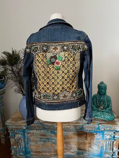 A lovely denim jacket that has been revamped using Indian trims and fabrics. The jacket is a vintage Levi jacket and in good condition. The main panel on the back is a vintage dress panel with embroidered mirror pieces all hand sewn. There are some new green and gold ribbon and decorative bead and sequinned vintage sari trim. There is a new floral patch in the centre.  The jacket measures around the chest 90 cms  The length from mid shoulder to the hem 55 cms. Bohemian Denim Jacket With Patches For Fall, Bohemian Cotton Denim Jacket With Patches, Bohemian Denim Jacket With Patches, Bohemian Patchwork Denim Jacket For Fall, Bohemian Embroidered Denim Jacket For Fall, Bohemian Denim Jacket With Floral Embroidery For Fall, Bohemian Cotton Denim Jacket With Floral Embroidery, Bohemian Embroidered Cotton Denim Jacket, Vintage Patchwork Denim Jacket For Festivals