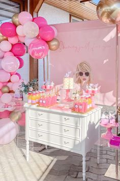 a table topped with lots of pink and gold balloons next to a white dresser covered in cake