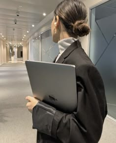 a woman standing in an office looking at her laptop computer while she is holding it