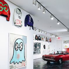 a red car parked in front of a white wall with pictures on it and lights hanging from the ceiling