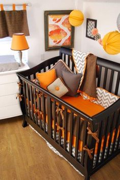 a baby crib is decorated with orange and brown pillows, chevron lamps, and decorative wall hangings