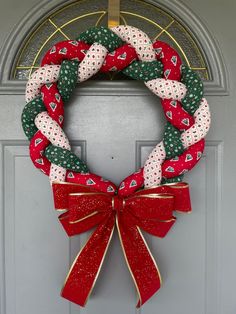 a christmas wreath hanging on a door with red and green ribbons tied around the wreath