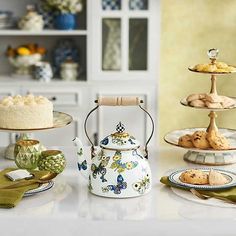 a tea kettle sitting on top of a white counter next to plates and cups filled with pastries