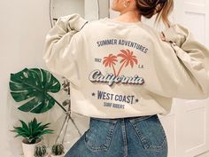 This cool retro California sweatshirt with palm trees design is the perfect gift idea or souvenir for every surfer in summer. Get yours now! Also available on t-shirts: https://www.etsy.com/listing/1044201694/retro-california-tee-california-tshirt Browse through my other awesome items here: http://thenims.etsy.com/ ABOUT THE PRODUCT: Unisex Heavy Blend™ Crewneck Sweatshirt | GILDAN 18000 (Customer Favorite) A sturdy and warm sweatshirt bound to keep you warm in the colder months. A pre-shrunk, c Trendy Summer Sweatshirt With Screen Print, Vsco Crew Neck Sweatshirt For Summer, Vsco Style Crew Neck Sweatshirt For Summer, Trendy Graphic Print Sweatshirt For Vacation, Oversized Summer Sweatshirt With Graphic Print, Trendy Summer Sweatshirt With Text Print, Summer Graphic Print Sweatshirt With Relaxed Fit, Summer Graphic Print Relaxed Fit Sweatshirt, Oversized Graphic Print Sweatshirt For Summer