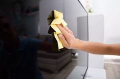 a person cleaning a television with a cloth on it's side and a hand holding a sponge over the screen