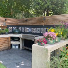 an outdoor kitchen with potted plants and flowers on the counter top, next to a wooden fence