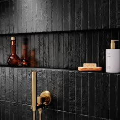 a black tiled bathroom with gold faucet and soap dispenser on the wall