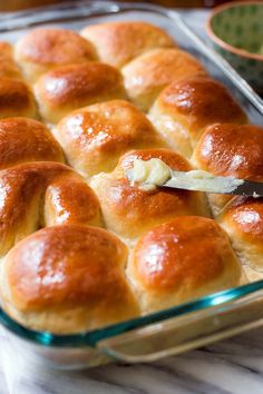 a glass baking dish filled with rolls and butter