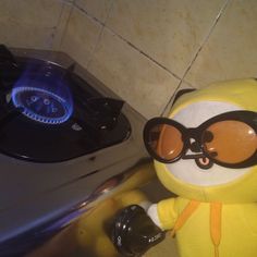 a yellow stuffed animal wearing sunglasses and holding a camera next to a stove top burner