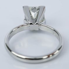 a white gold engagement ring with a princess cut diamond in the center, on a plain surface