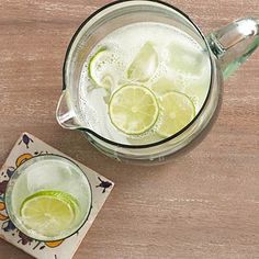 a pitcher filled with ice and limes on top of a wooden table next to a napkin