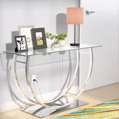 a glass and metal console table with pictures on it's shelf next to a rug