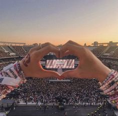 two hands making a heart shape in front of a large crowd at a football game