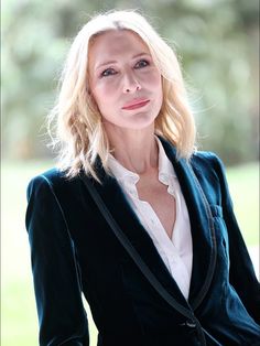 a woman with blonde hair wearing a black jacket and white shirt is posing for the camera