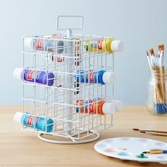 a rack with paint and brushes on a wooden table next to a plate full of watercolors