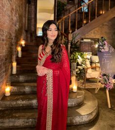 a woman in a red sari standing next to some stairs with candles on either side