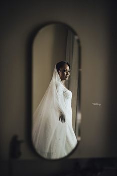 a woman in a wedding dress is looking at herself in the mirror while wearing a veil