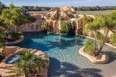 an aerial view of a swimming pool surrounded by palm trees and rocks in the background