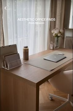 an office desk with a laptop and other items on it, in front of a window