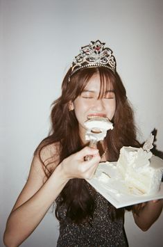 a woman wearing a tiara eating a piece of cake with icing on it