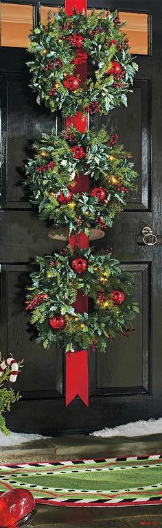 a decorated christmas tree in front of a black door with red bows and ornaments on it