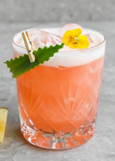 a pink drink with yellow flowers on the rim and green leafy garnish