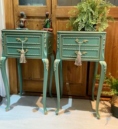 two green nightstands with tasseled drawers in front of a wooden door and potted plant