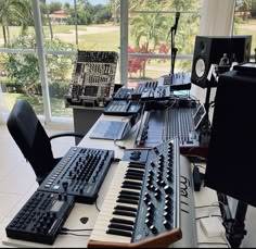 there are many electronic keyboards on the table in front of the window, and one keyboard is black