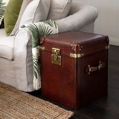 a brown trunk sitting on top of a wooden floor next to a white couch and green pillows