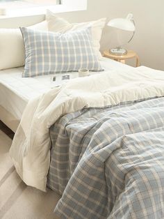 a bed with blue and white checkered comforter on top of it next to a window