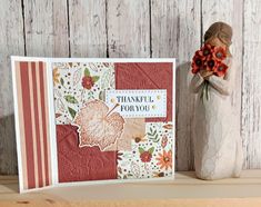 a vase with flowers and a thank you card on top of a wooden shelf next to it