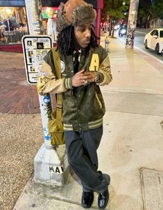 a man with dreadlocks standing next to a pole and looking at his cell phone