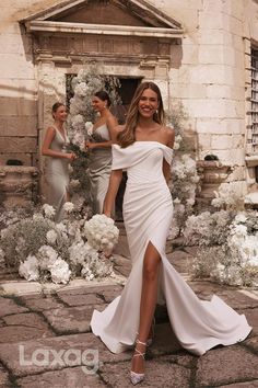 a woman in a white dress standing next to two other women and one is holding flowers