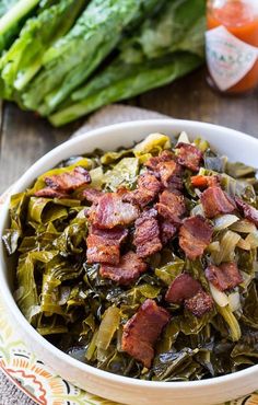 a bowl filled with bacon and collard greens on top of a table next to vegetables