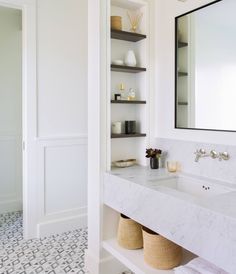 a bathroom with white walls and marble counter tops, along with open shelving on the wall