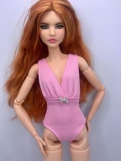 a doll with long red hair wearing a pink swimsuit and holding her hands on her hips