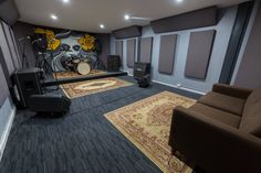 a room with two chairs, a couch and a drum set on the floor in front of a large mural