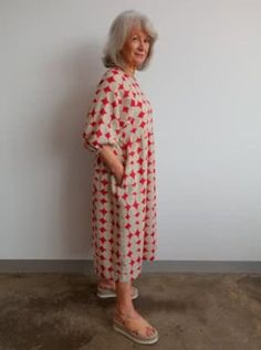 an older woman standing in front of a white wall wearing a red and white dress