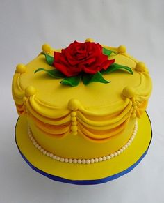 there is a yellow cake with a red rose on top and pearls around the edges