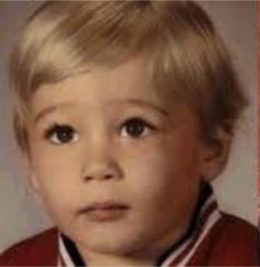 an old photo of a young boy with blonde hair and brown eyes, wearing a red sweater