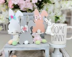 some bunny figurines are sitting on a small table next to a coffee mug