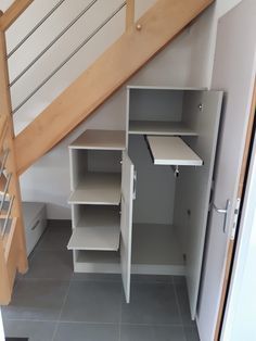 an open closet under the stairs in a room with gray tile flooring and wooden handrails