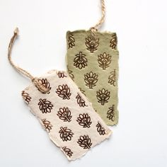 two tags with designs on them hang from twine strings against a white background, one is green and the other is brown