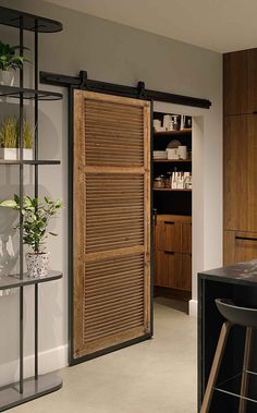 an open sliding door in a kitchen next to a bar with stools and shelves