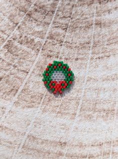 a red and green beaded brooch sitting on top of a white cloth covered floor