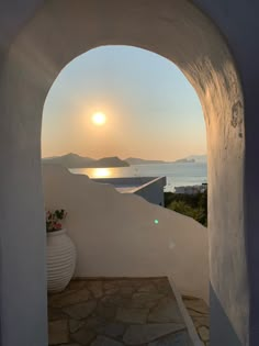 the sun is setting through an arch in a building with a view of water and mountains