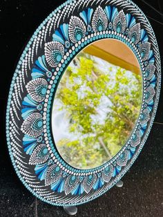 a blue and white mirror sitting on the side of a wall next to a tree