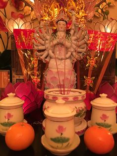 an assortment of decorative items displayed in front of a statue and oranges on a table