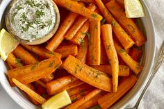 a bowl filled with carrots and lemon wedges next to a small dipping sauce