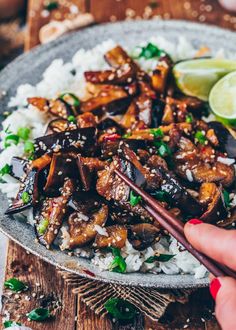 someone is holding chopsticks over rice with eggplant and mushrooms on it